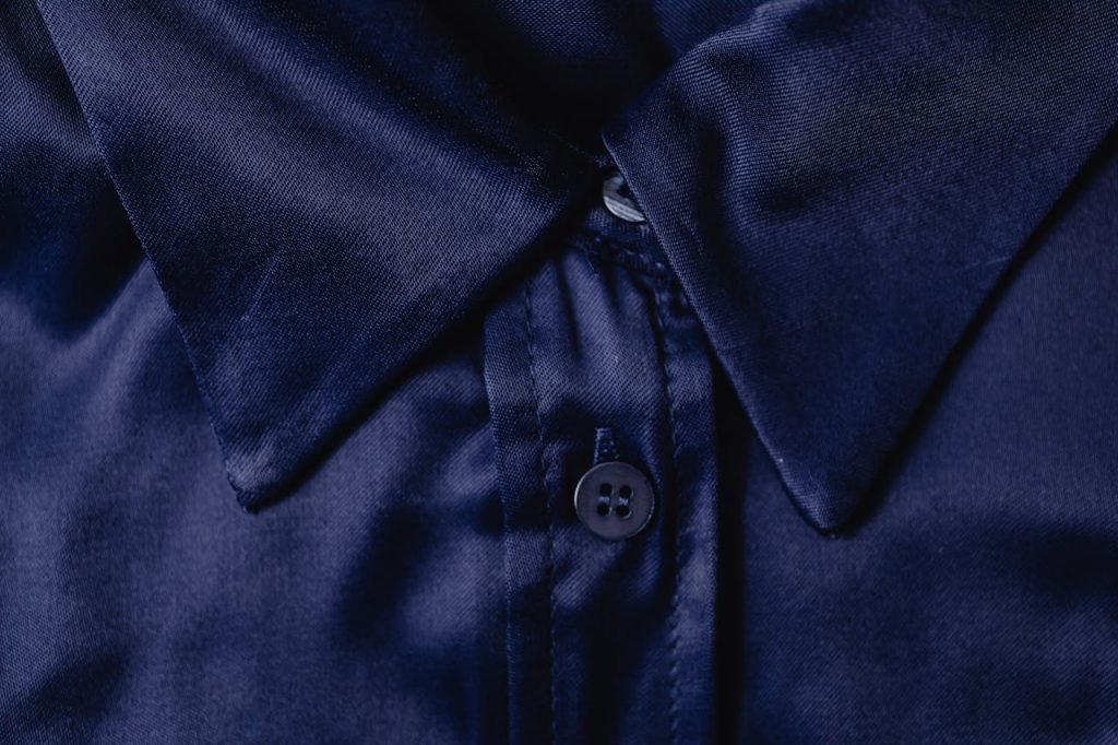 Detailed close-up of a blue silk shirt collar highlighting fabric texture and button.