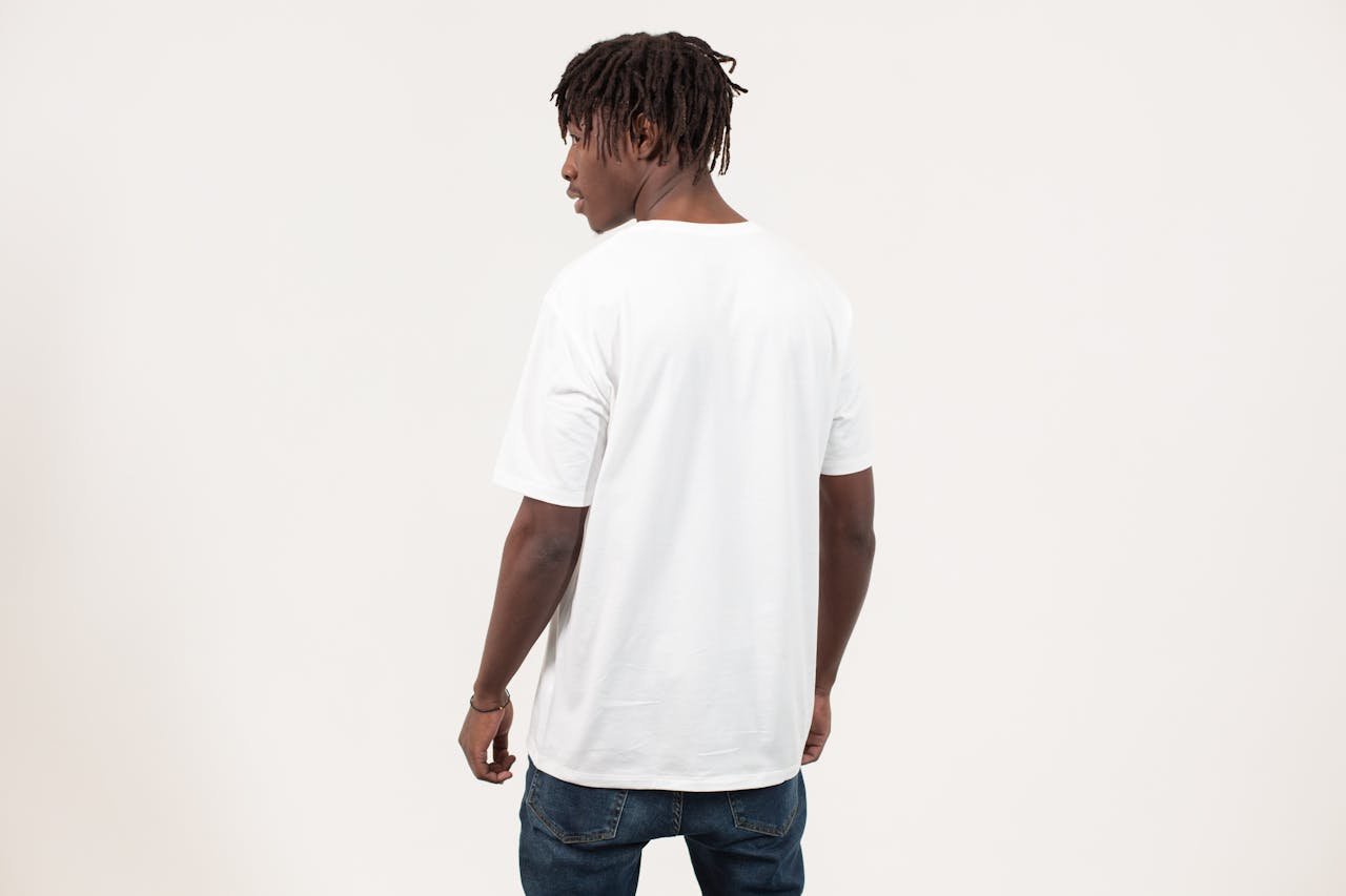 Back view of serious young African American guy with dreadlocks in casual t shirt standing against white background and looking away